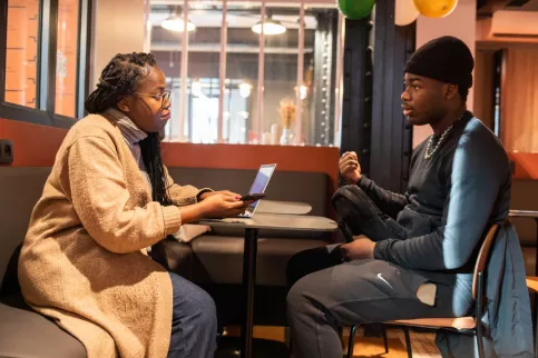 Un jeune assis face à son accompagnatrice à une table, ils dicustent