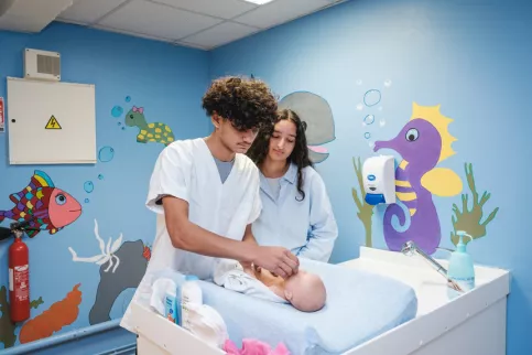Deux jeunes en formation SAPAT s'occupent d'un bébé en salle de puériculture