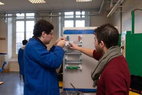 Un jeune et son formateur en électricité travaillent sur un plateau technique