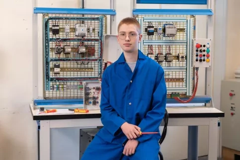 Jeune en formation électricité posant devant son plateau technique de formation