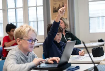 Jeunes collégiens en classe, l'un lève la main, l'autre est sur un ordinateur
