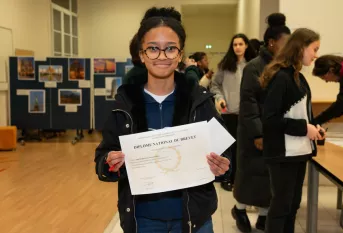 Jeune fille souriante tenant son Diplome du Brevet devant elle 