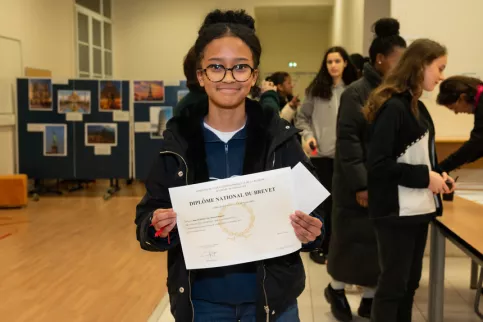 Jeune fille souriante tenant son Diplome du Brevet devant elle 