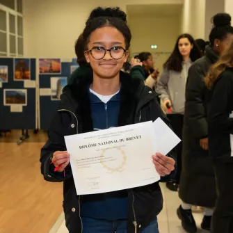 Jeune fille souriante tenant son Diplome du Brevet devant elle 