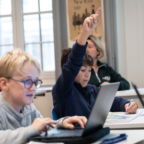 Jeunes collégiens en classe, l'un lève la main, l'autre est sur un ordinateur