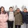 Quatre enfants, trois garçons et une fille bras dessus bras dessous regardent la caméra 