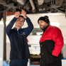 Jeune en formation mécanique automobile travaillant sous une voiture en hauteur avec son formateur