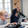Jeunes collégiens en classe, l'un lève la main, l'autre est sur un ordinateur
